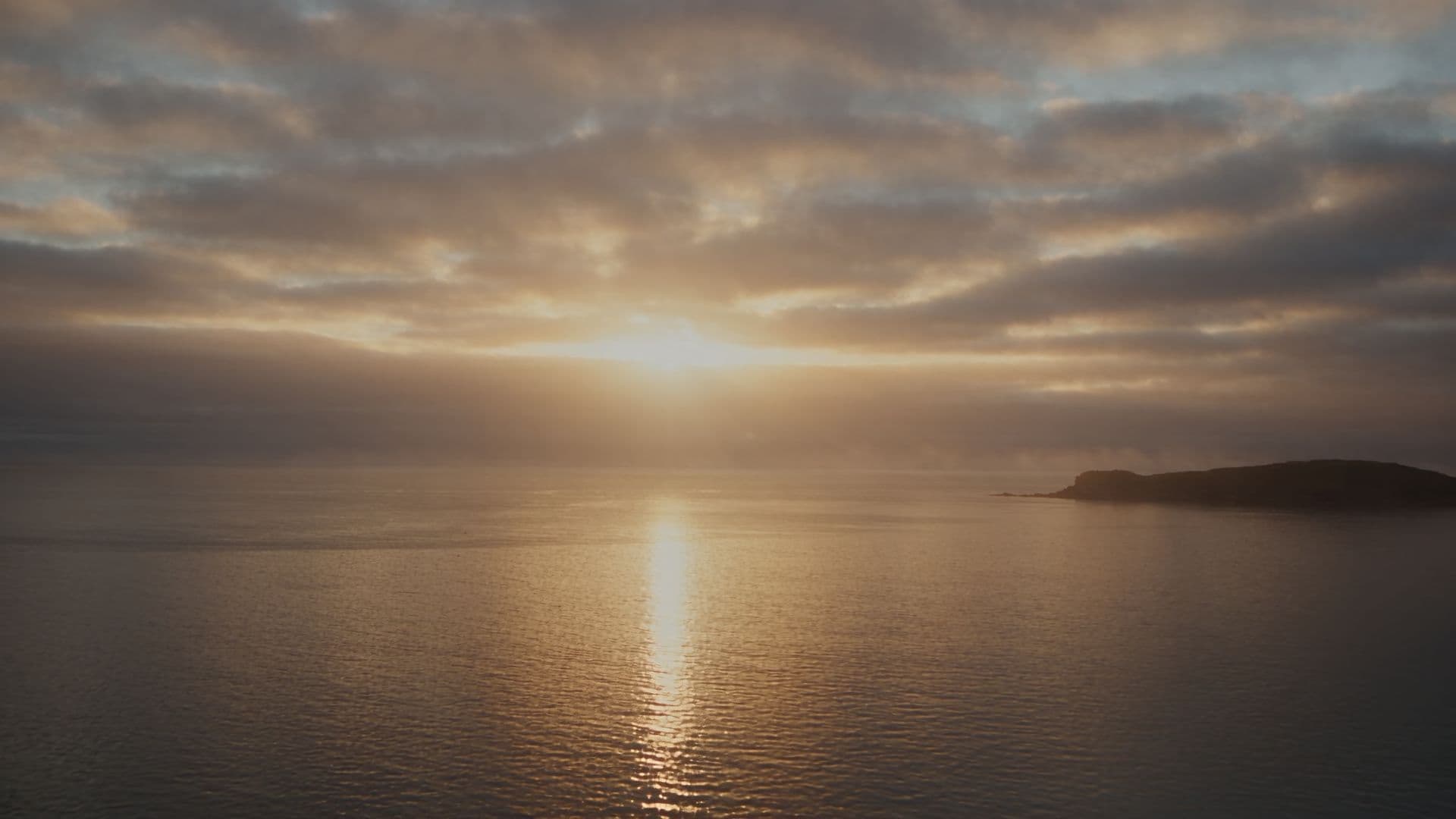 Sunrise breaking through clouds over a calm bay